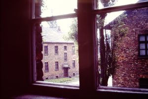 The view of two brick barracks buildings from inside the window of a third in 1977 Auschwitz