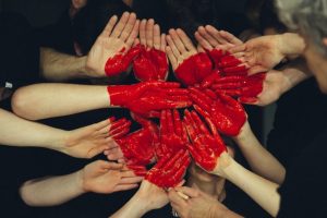 Hands crowded together with a red heart painted on them