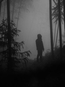 Black and white photo of a person standing in foggy woods