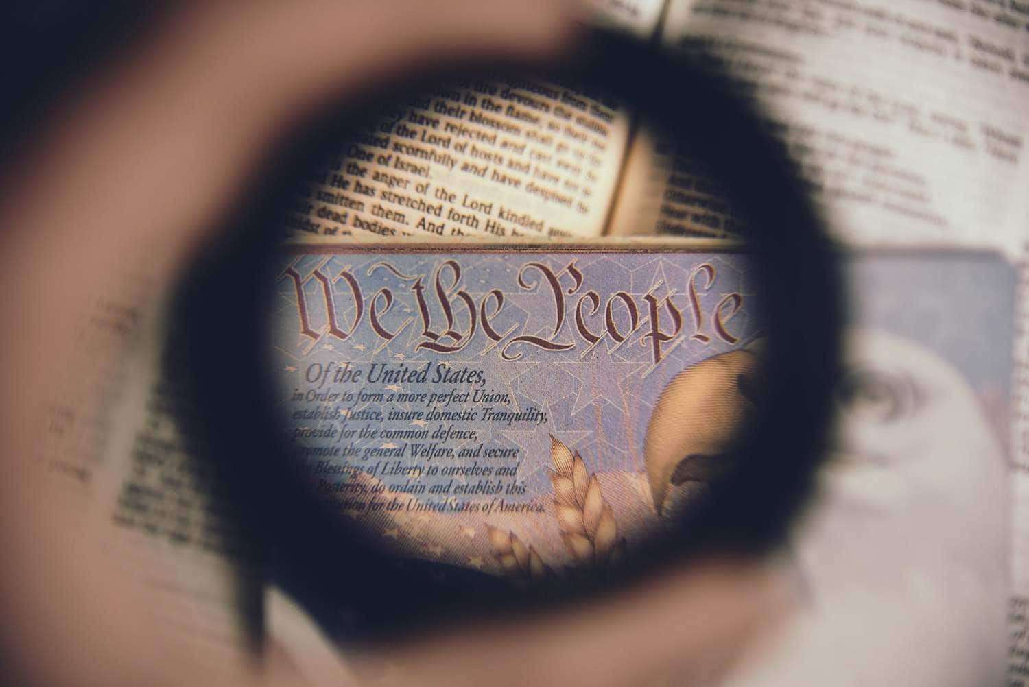 Looking through a magnifying lens, "We the People" from a copy of the U.S Constitution is visible over an open Bible