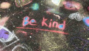 Words on sidewalk say Be Kind in chalk.