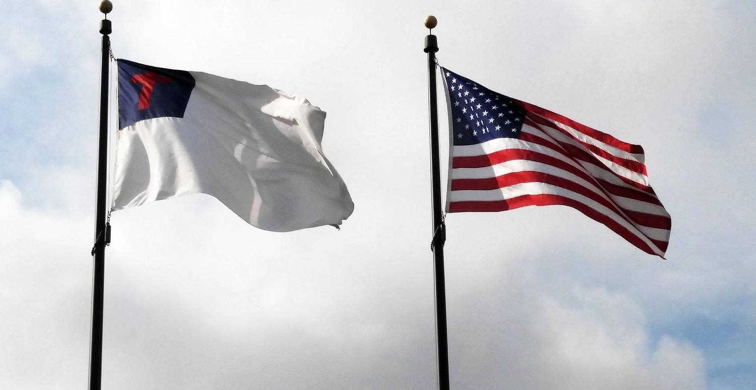 Christian flag (white with blue field in upper left containing a red Roman cross) and a US flag flying side by side on poles.