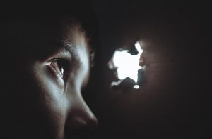 child in the dark looking through a hole to the light