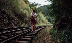 girl with backpack walking away on train tracks