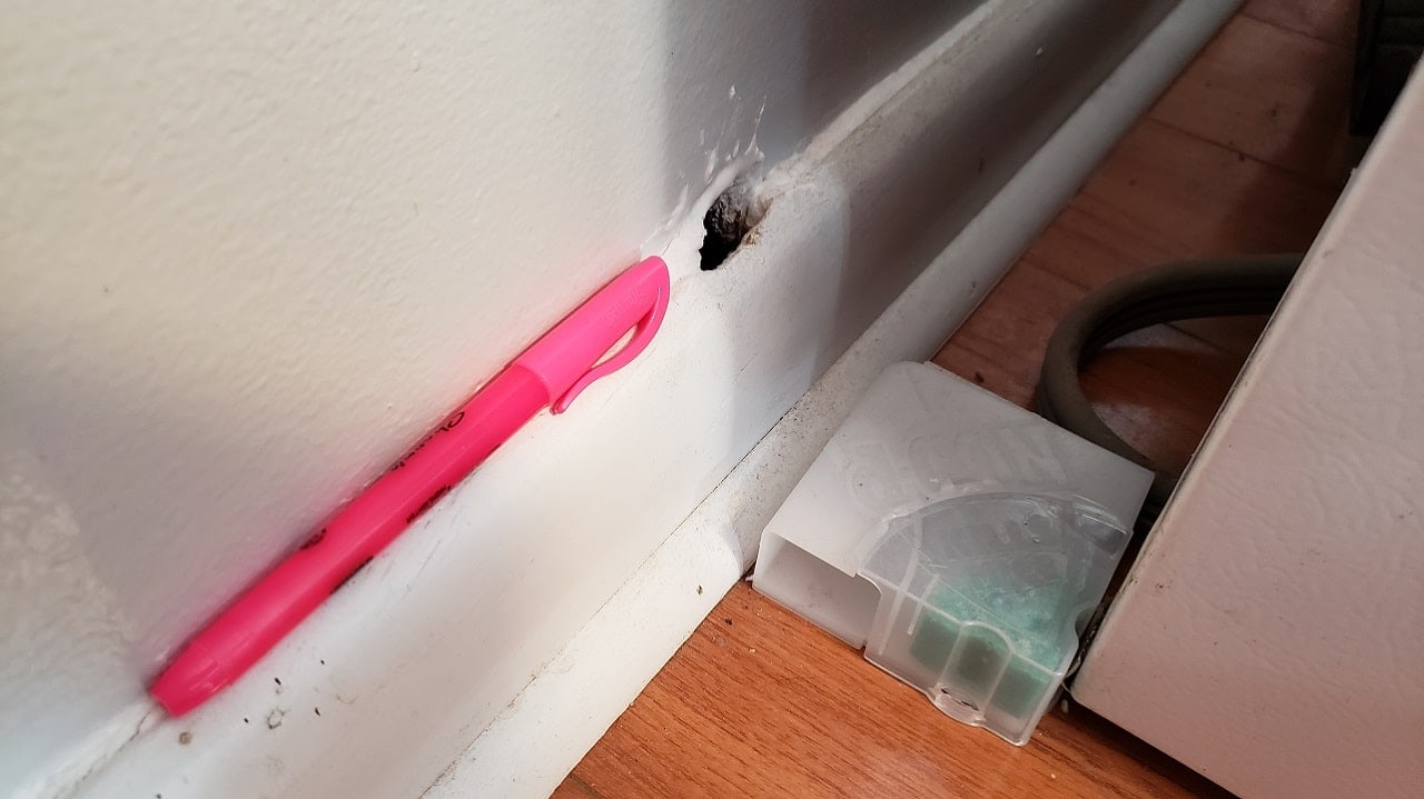 Photo of hole in base of a wall with pink highlighter next to it for scale
