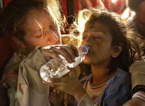 woman in desert camo giving young girl water from a bottle