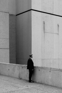 Black and white photo of a man standing among tall concrete buildings 