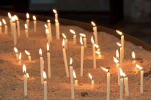 Many lit candles in a tray of sand